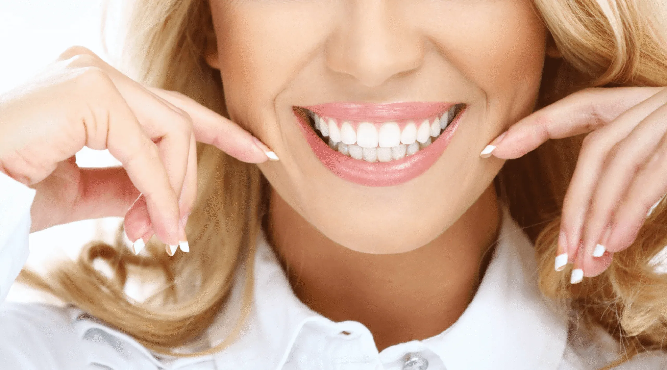 Woman smiling broadly and gently pulling the corners of her mouth outward to show her teeth.